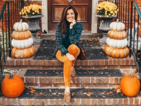 Woman in orange pants and plaid shirt on a pumpkin-lined stoop