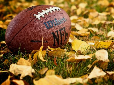 An American football resting on a field with yellow leaves